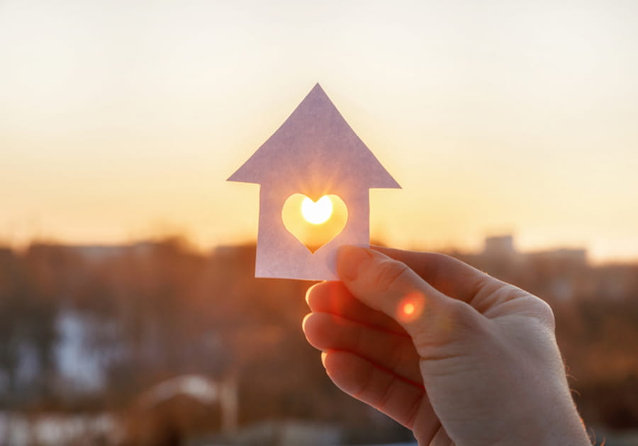 Person holding up paper cutout of a house with a heart in it.