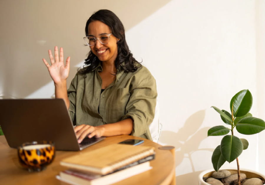 Person smiling and waving at a laptop screen