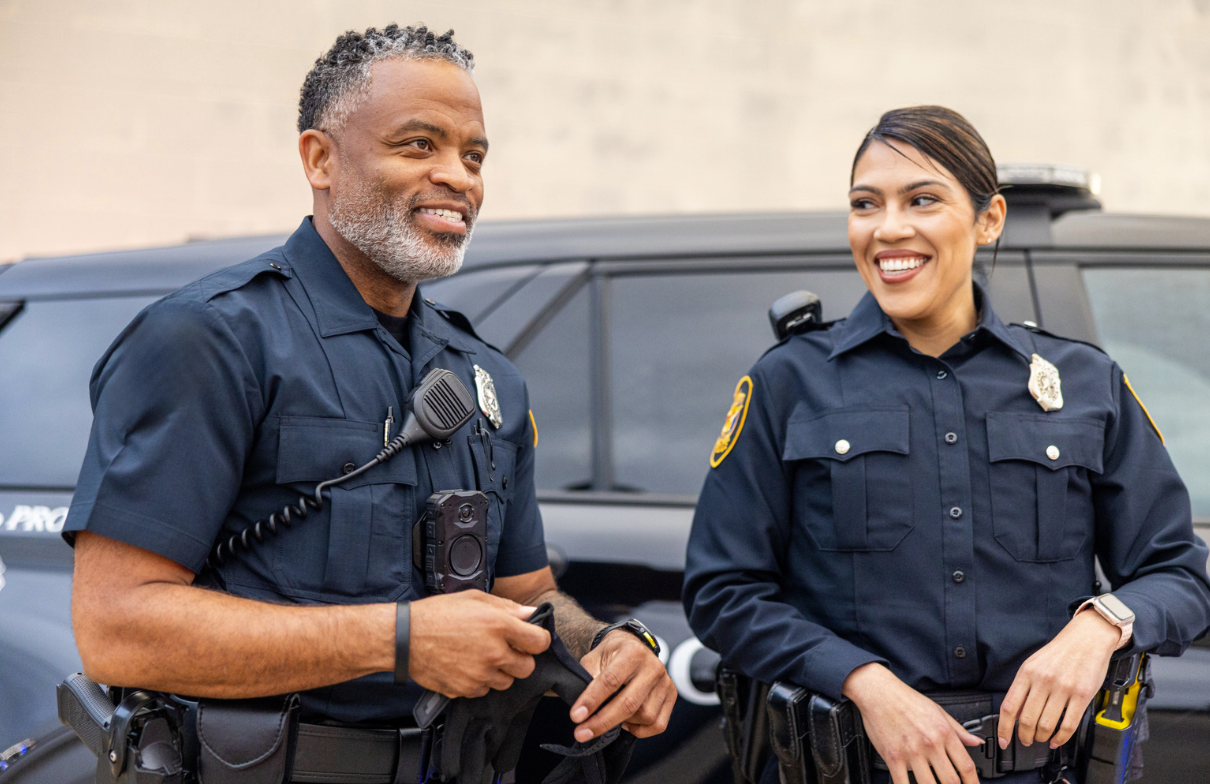 Two smiling Halton Regional Police officers standing beside a police vehicle
